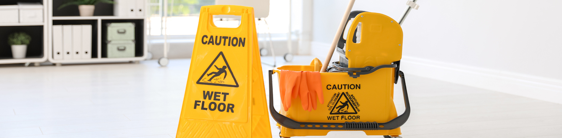 A janitorial mop bucket with a wet floor caution sign next to it